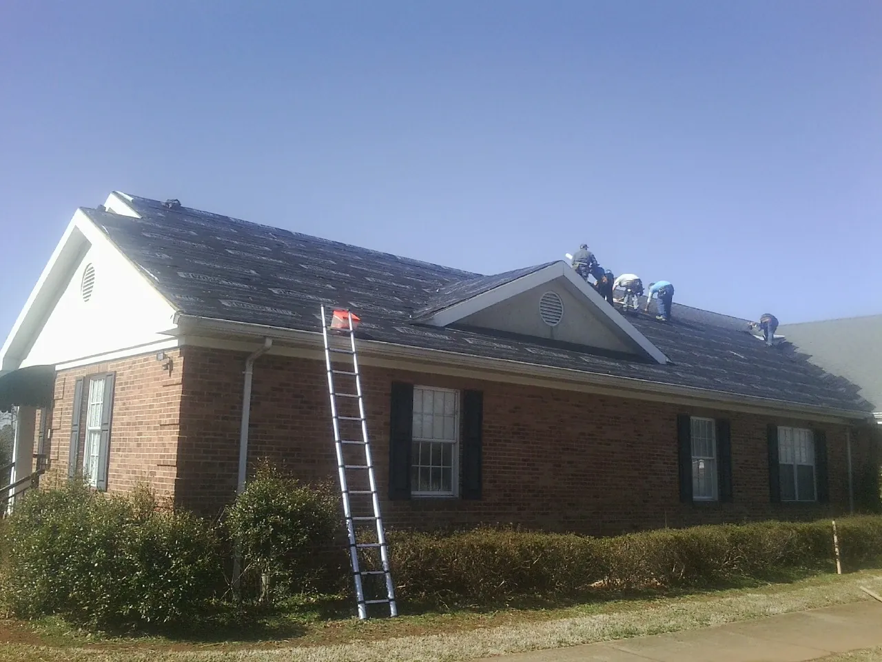 Crew tearing shingles off a brick ranch roof with a ladder set — Emergency Roof Repair work by our crew in Lonaconing