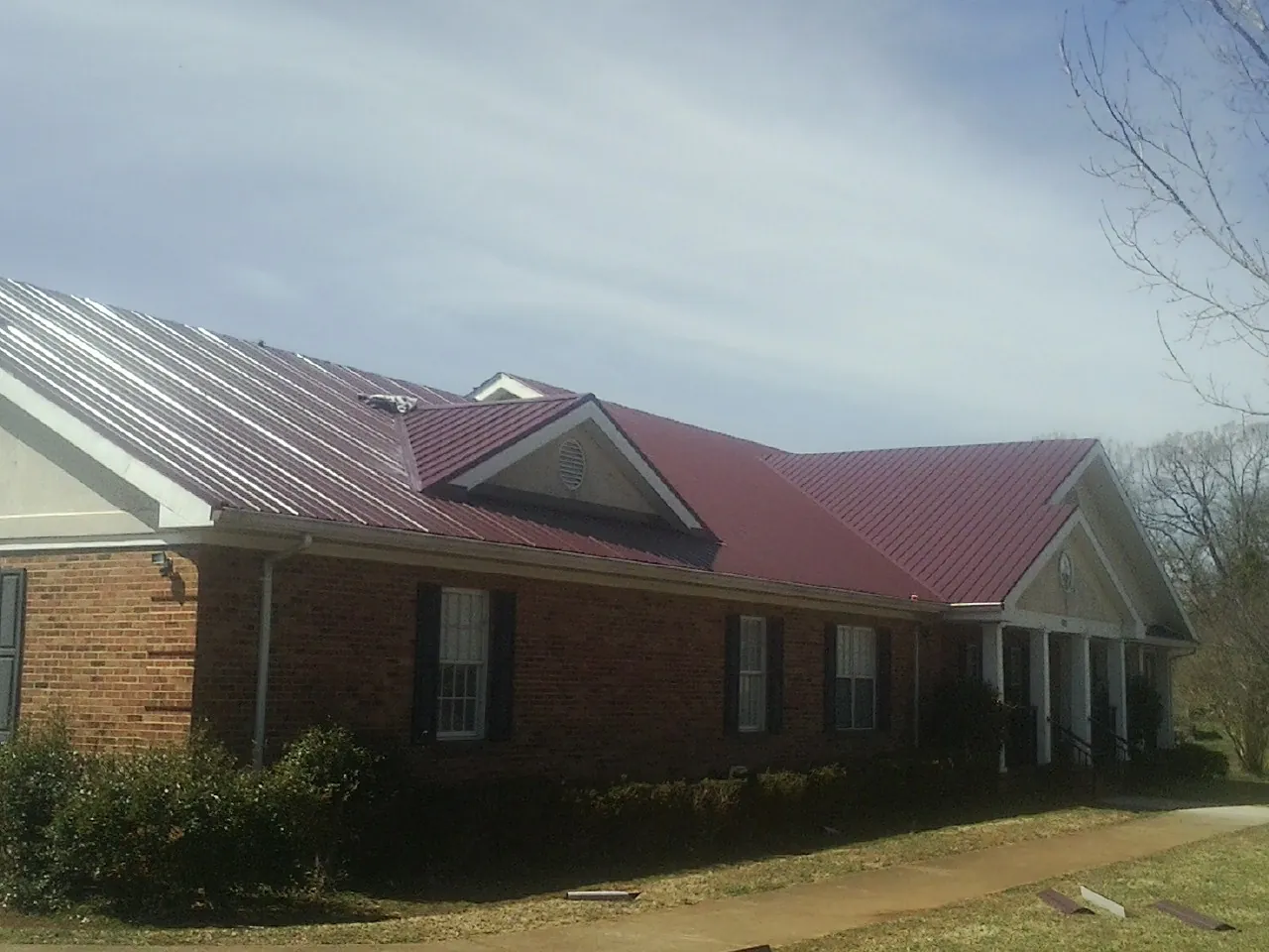 Red metal roof with gabled entries on a long brick building, from a Hail Damage Roof Repair job in Lonaconing