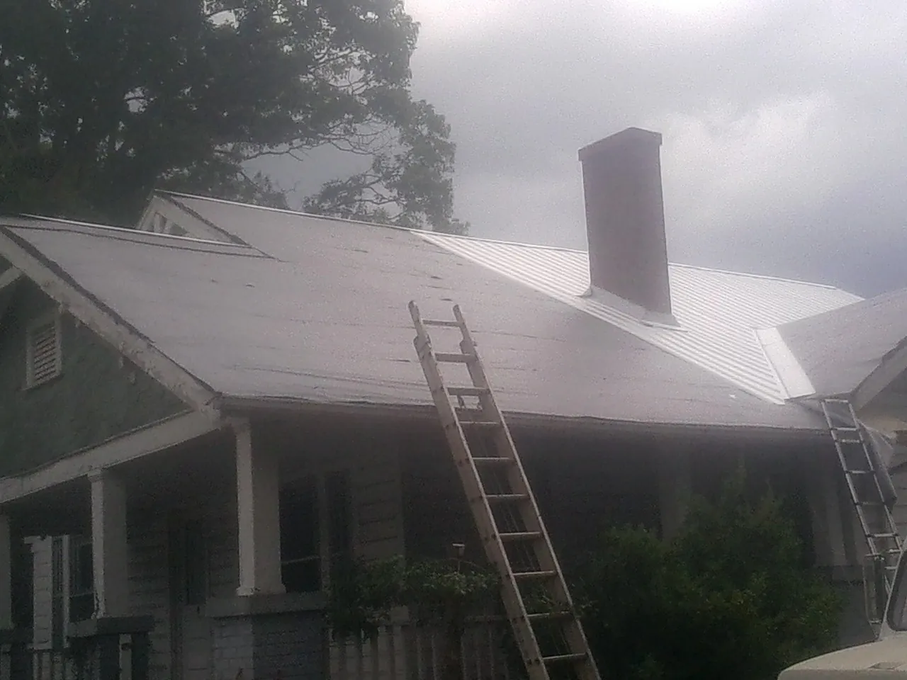 Ladders against a metal roof on an older home with a brick chimney in Lonaconing