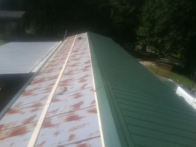 Old rusted panels beside newly installed green metal roofing — Wind Damage Roof Repair by Roofing Brothers in Lonaconing