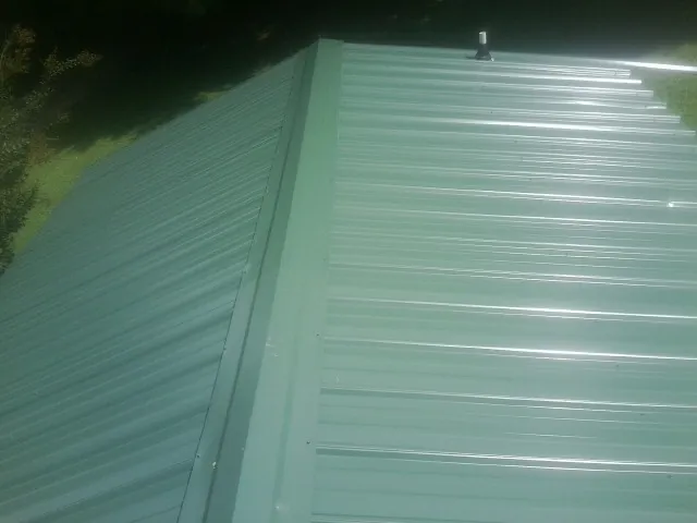 New green metal panels meeting at the ridge of a roof — Flat Roof Repair work by our crew in Lonaconing