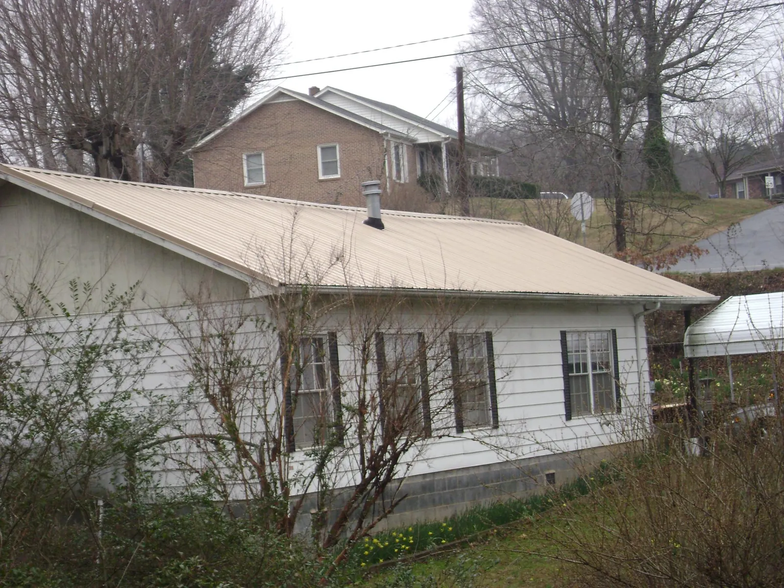 Tan metal roof on a white sided house set into a hillside — Commercial Roofing by Roofing Brothers in Lonaconing