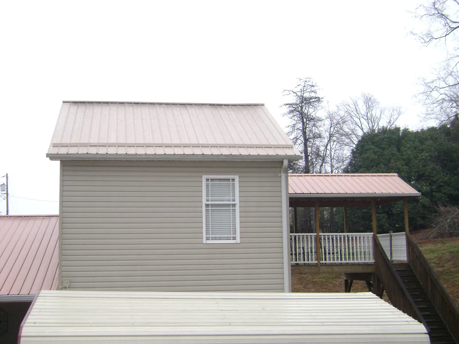 Tan metal roofs on a two story addition and attached porch, from a Roof Replacement job in Lonaconing